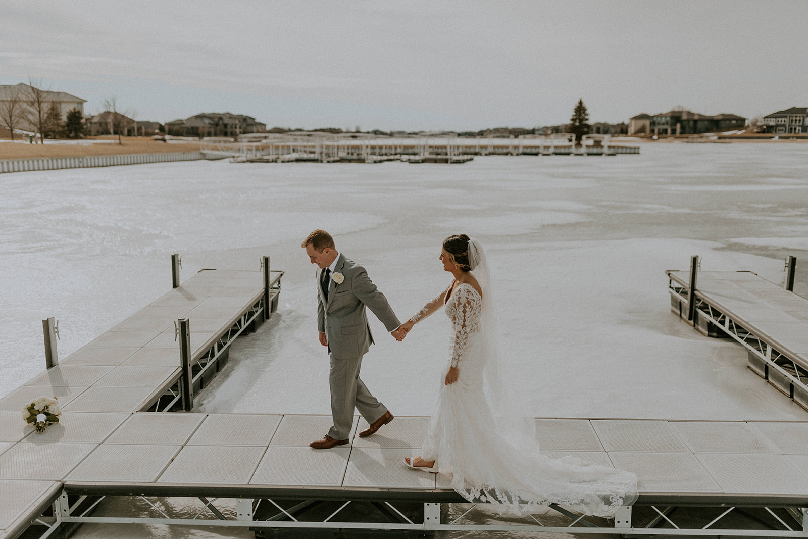 Bride and groom holding hands as they walk on the dock with a lake view, captured by McKenna Christine Photography