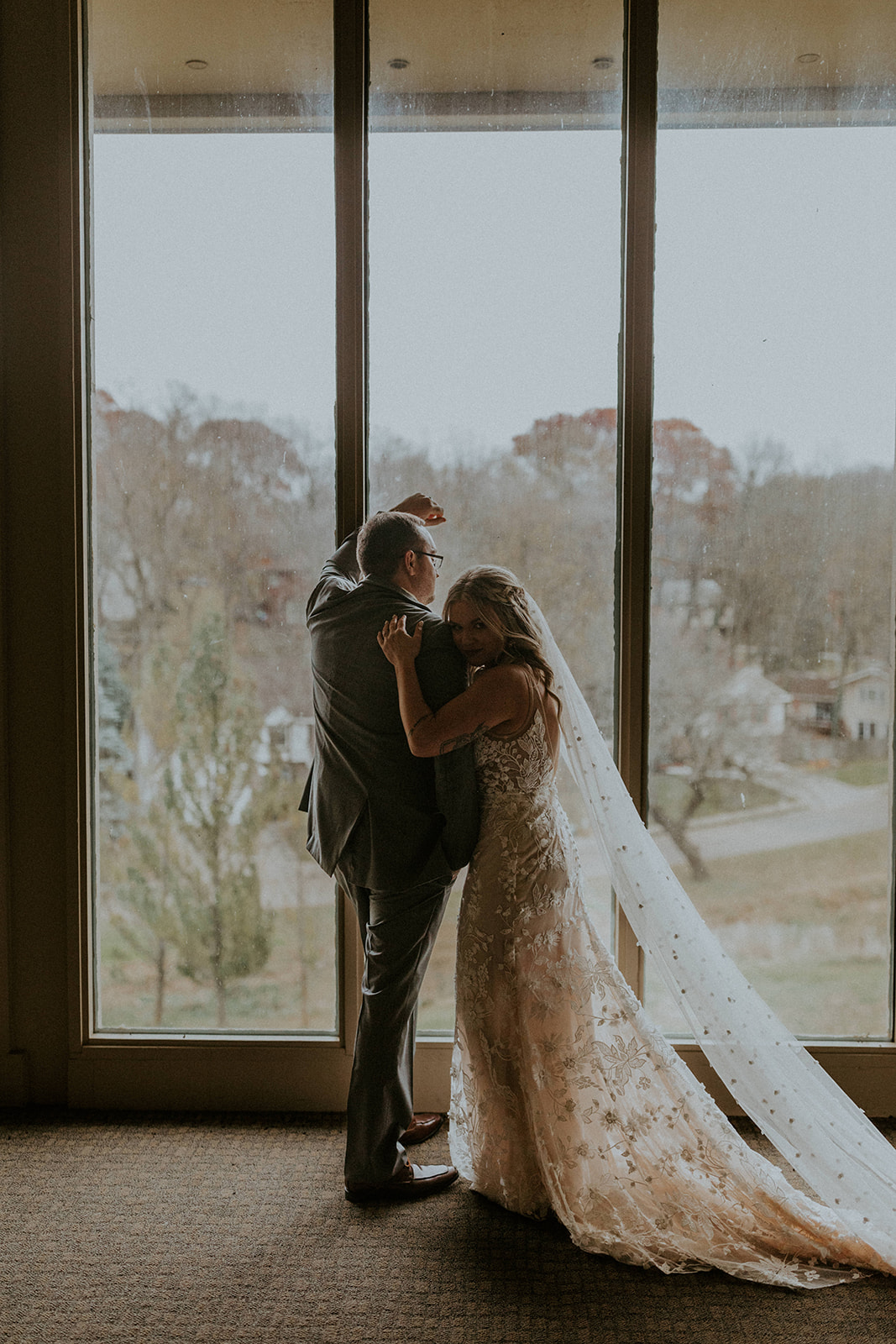The Most Sought After Wedding Venues in Omaha, Nebraska: Bride hugs groom as he leans against the window.
