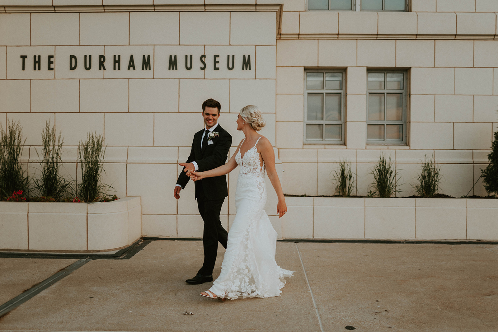 Bride and groom smiling at each other while holding hands and walking past the The Durham Museum sign in Omaha, Nebraska