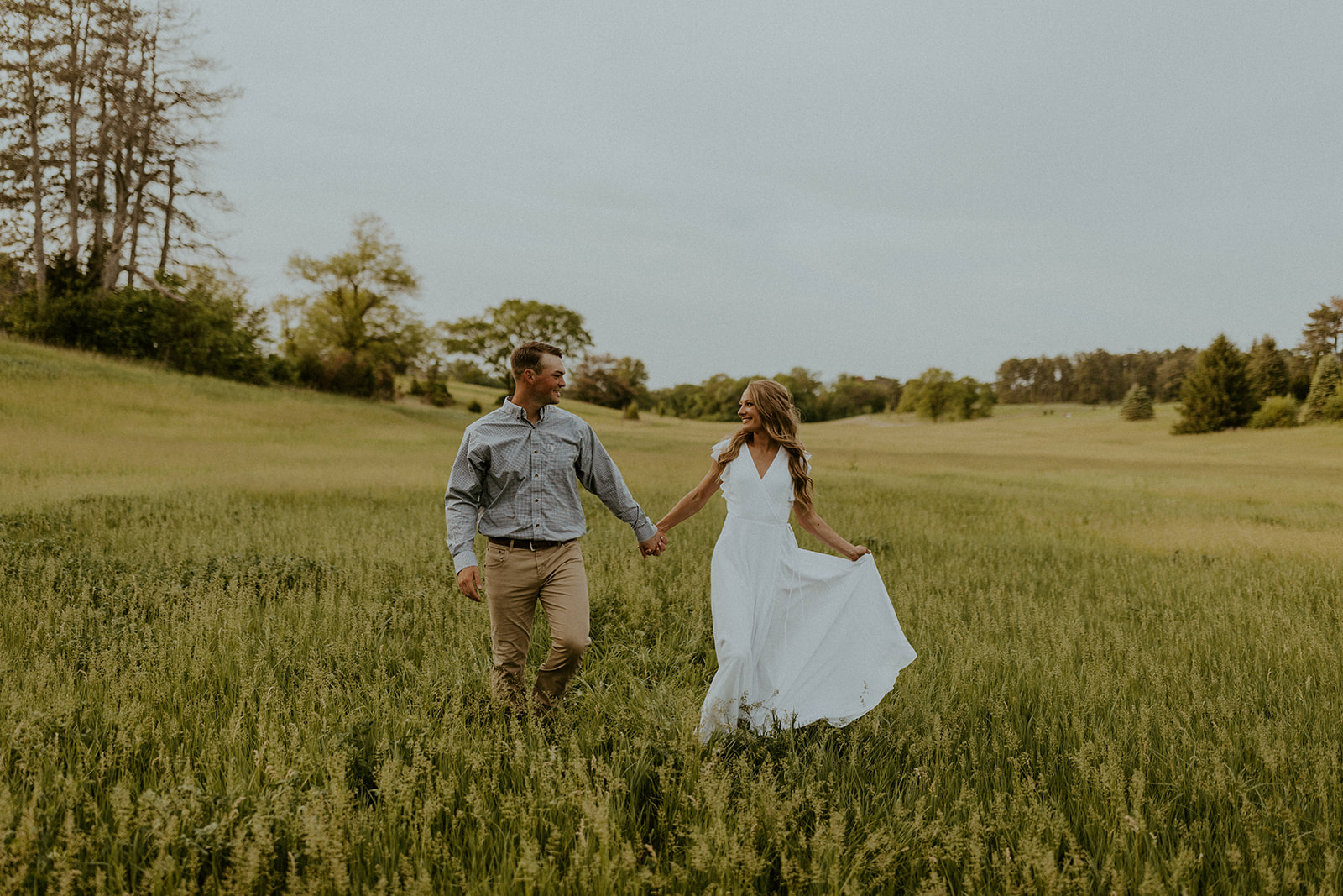 7 Engagement Photo Tips For The Perfect Engagement Session: Couple hold hands and smile at each other in the middle of a field.
