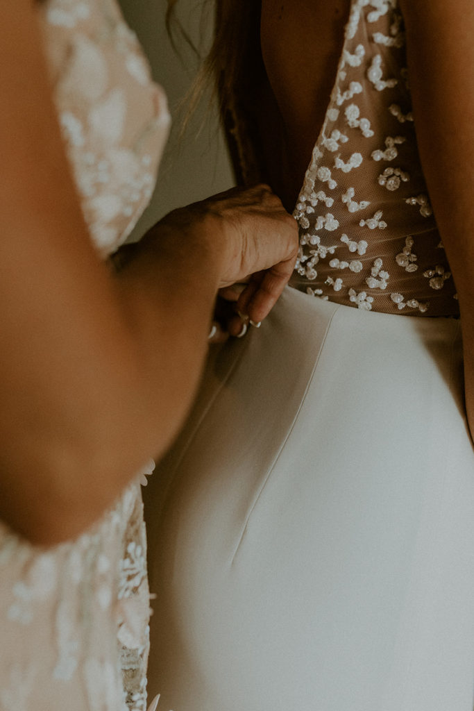 Close-up shot of bridesmaid securing the back of bride's dress, taken by McKenzie Christine Photo