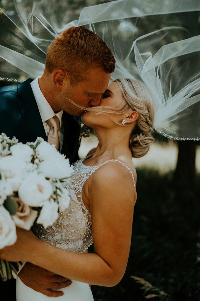 Bride and groom sharing a kiss as bride holds her white bouquet, captured by McKenna Christine Photography