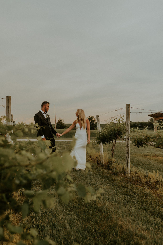 Bride and groom holding hands as they walk through the yard at Glacial Till Vineyard