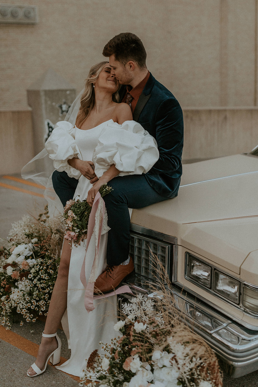 How to Choose A Wedding Photographer That's Perfect For You. Groom sits on hood of car and embraces bride.