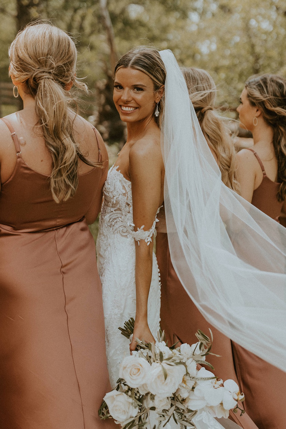 Bride looking back and smiling at the camera next to her bridesmaids, shot by elegant wedding photographer McKenna Christine