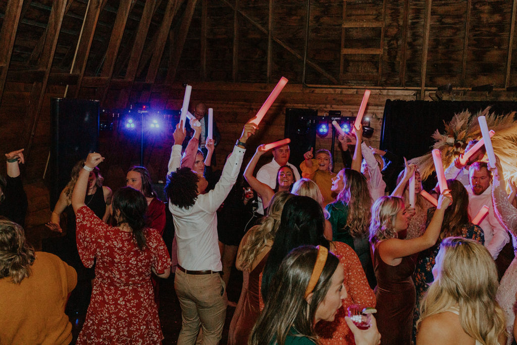 19 Non-Traditional Wedding Ideas To Make Your Wedding Day Uniquely Yours. Glowsticks held up by guests dancing at wedding reception.