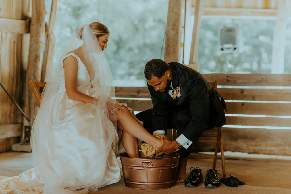 Groom crouching down to wash bride's feet during their traditional wedding ceremony, taken by McKenna Christine Photography