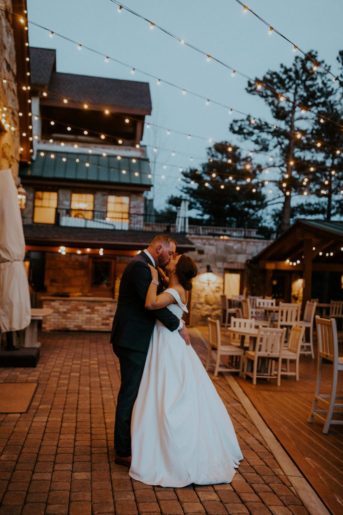 Bride and groom sharing a kiss at the reception venue with string lights overhead, taken by McKenna Christine Photography