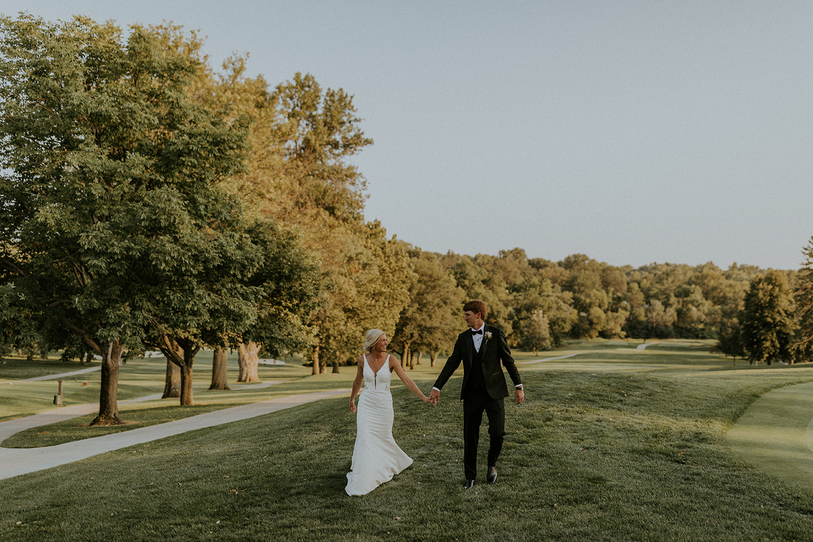 Bride and groom holding hands as they walk around the golf course, captured by McKenna Christine Photography