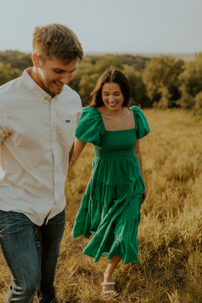 Guy holding his fiance's hand as they walk through the grass, taken by McKenna Christine Photography