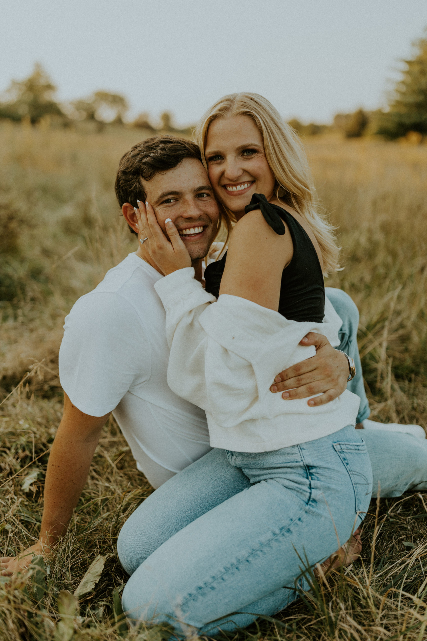What to Wear For Engagement Photos + What NOT to Wear. Engaged couple smiling at the camera while sitting on the grass.
