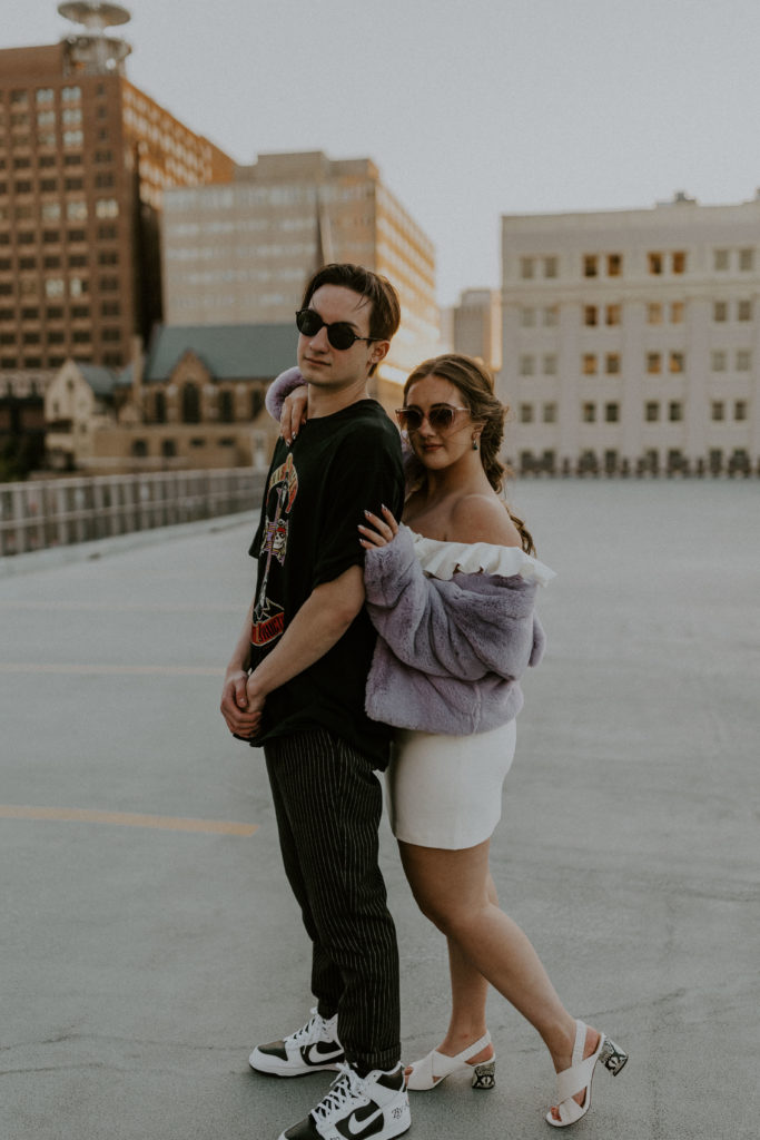 Engaged couple smiling at the camera as they pose with their sunglasses, taken by McKenna Christine Photography